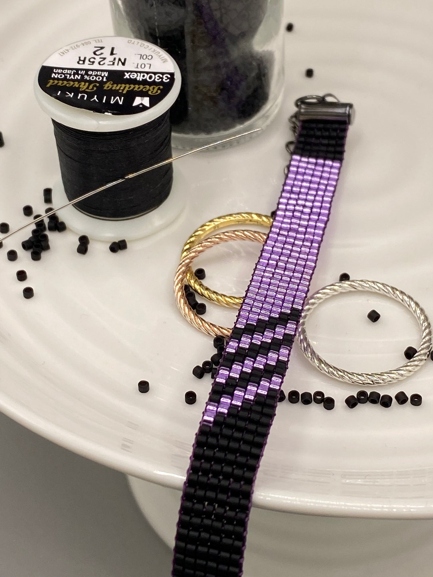 Purple beaded bracelet with black beads on a white surface, surrounded by a spool of black thread.