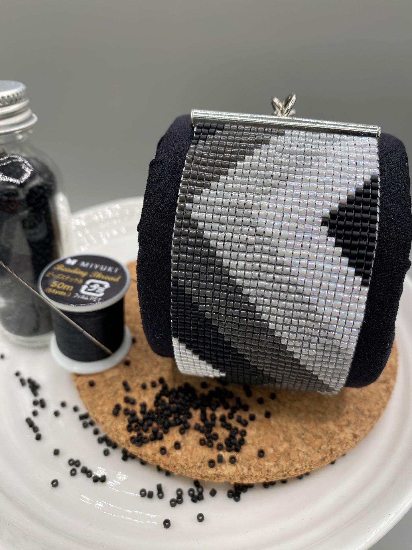 Close-up of a black, grey, and white beaded bracelet with chevron pattern on a cork and white plate.