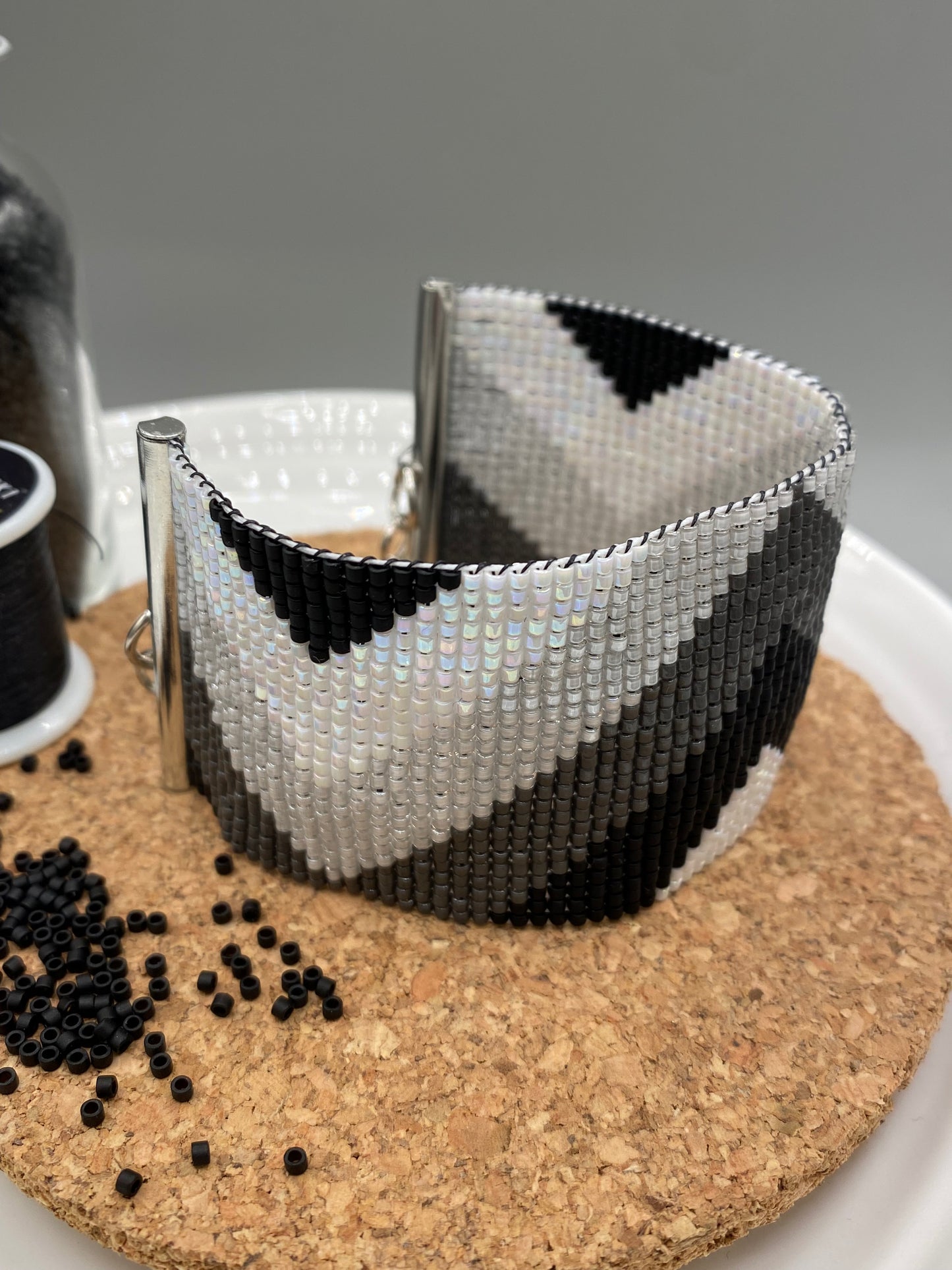 Close-up of a black, grey, and white beaded bracelet with chevron pattern on a cork and white plate.