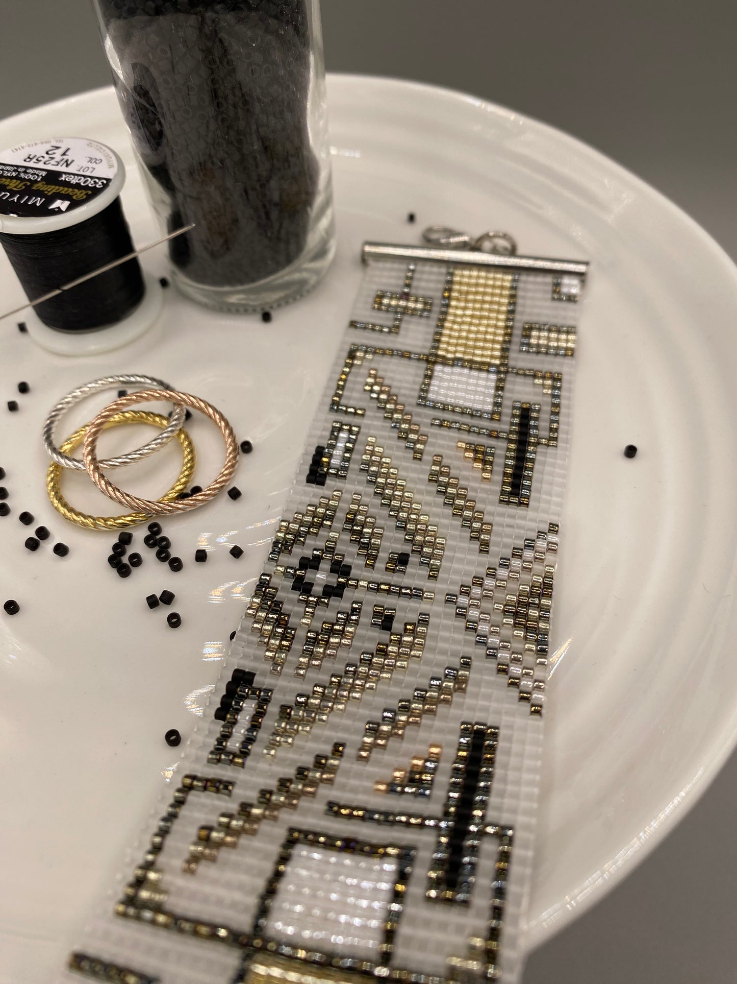 Close-up of a beaded cuff bracelet with intricate pattern on a white plate surface.