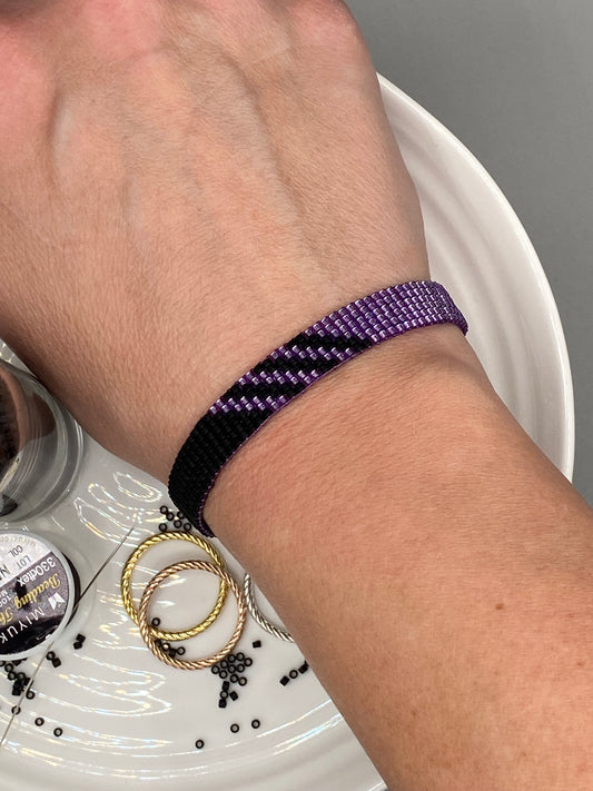 Hand wearing a purple beaded bracelet resting on a white plate.
