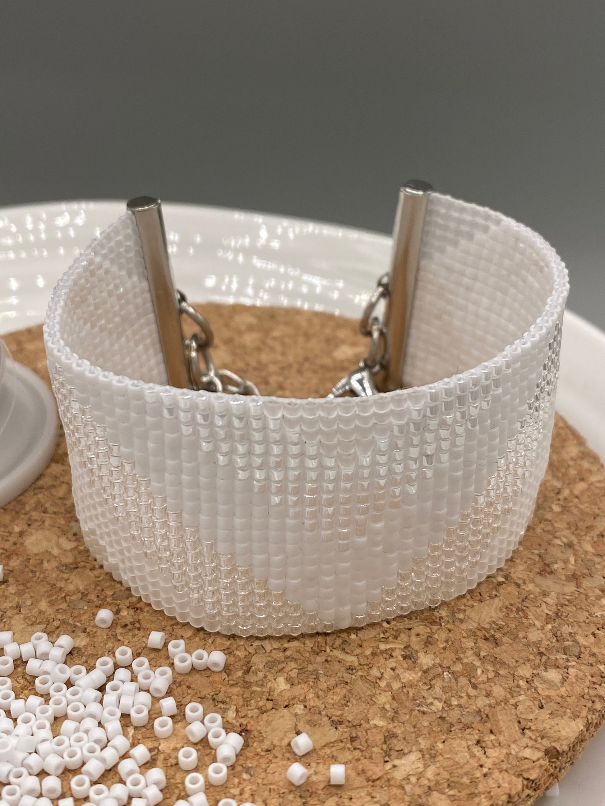 Close-up of a white, pearl, and crystal beaded bracelet with chevron pattern on a cork and white plate.