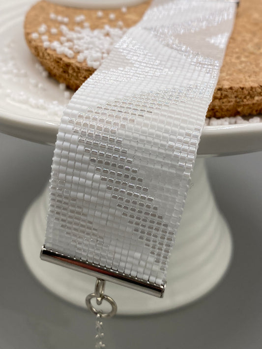 Close-up of a white, pearl, and crystal beaded bracelet with chevron pattern on a cork and white plate.