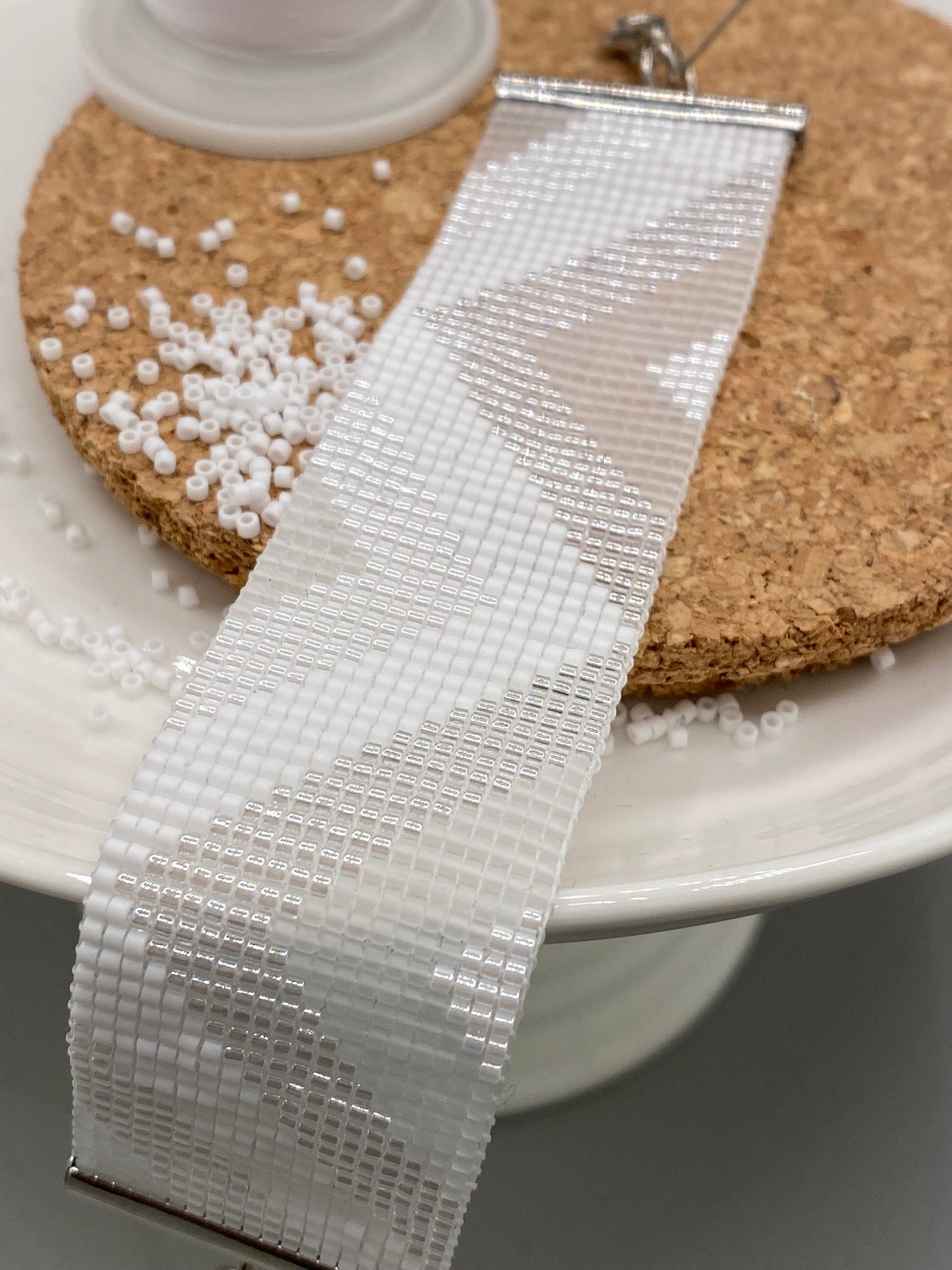 Close-up of a white, pearl, and crystal beaded bracelet with chevron pattern on a cork and white plate.