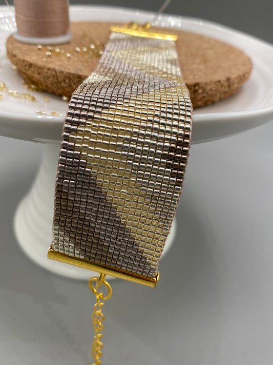Gold beaded bracelet with a chevron pattern on a white and cork plate with a blurred background.