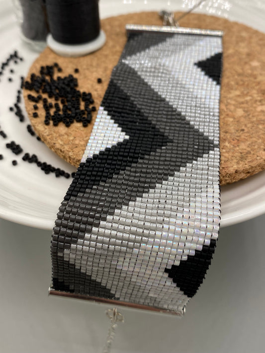 Close-up of a black, grey, and white beaded bracelet with chevron pattern on a cork and white plate.