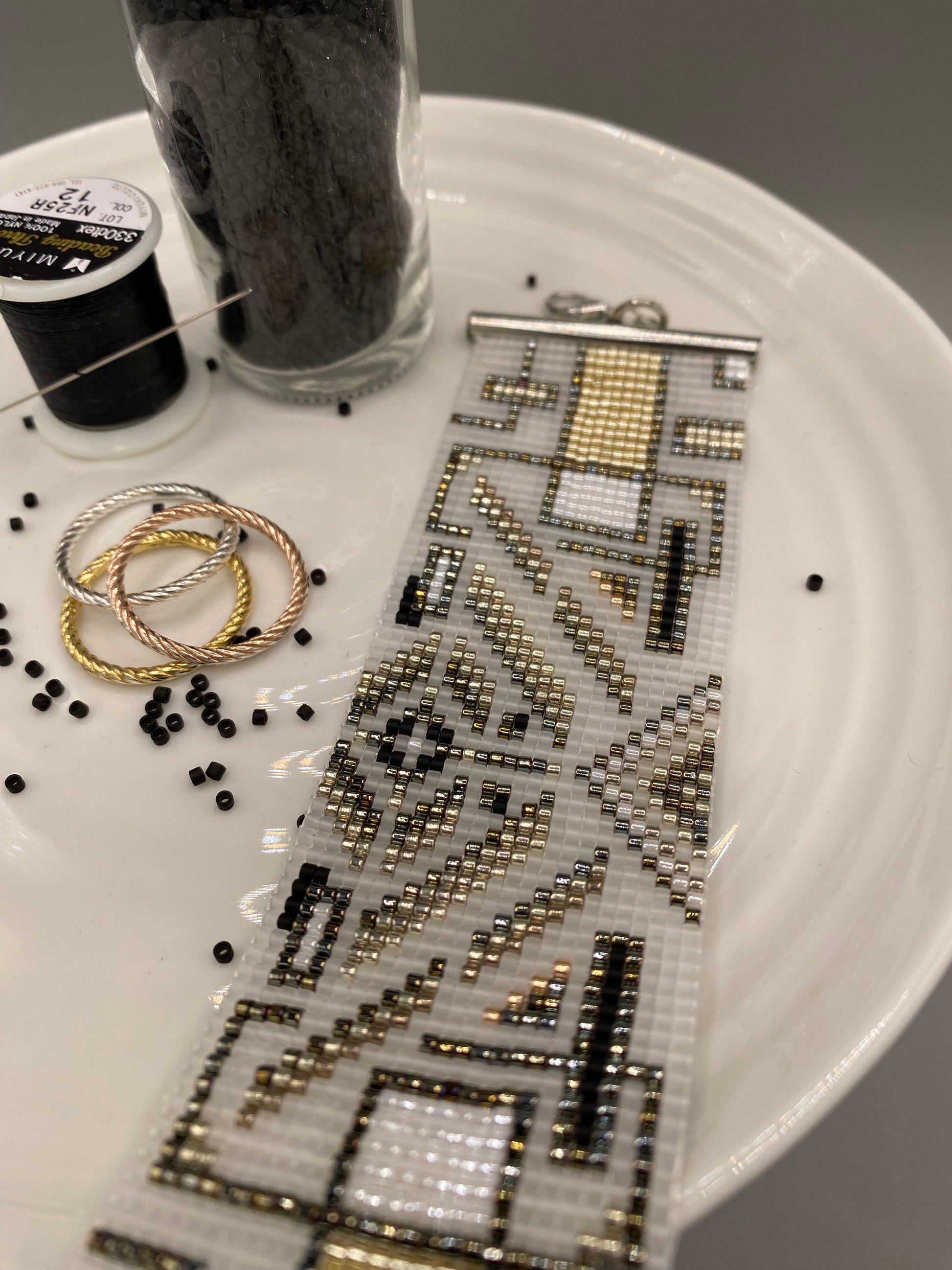 Close-up of a beaded cuff bracelet with intricate pattern on a white plate surface.