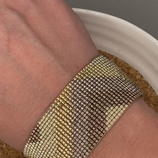 Video of a gold beaded bracelet with a chevron pattern on a white and cork plate.