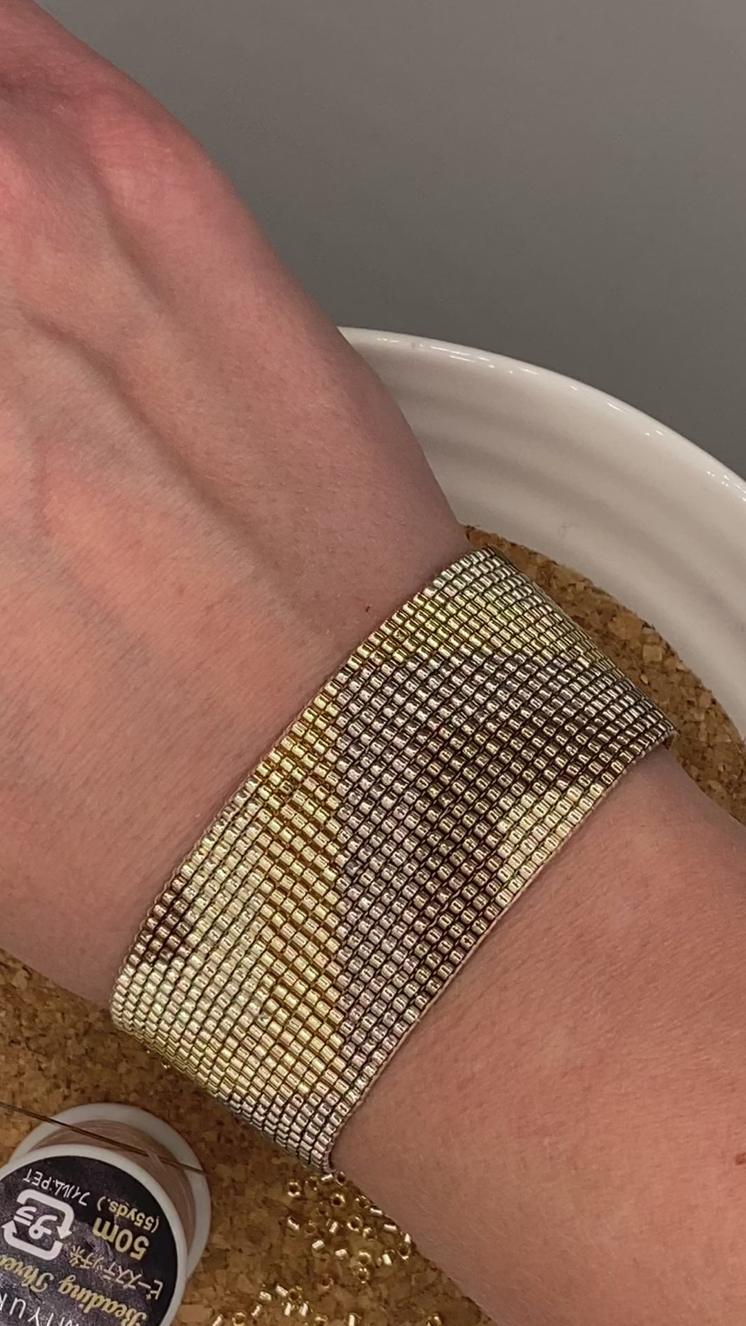 Video of a gold beaded bracelet with a chevron pattern on a white and cork plate.