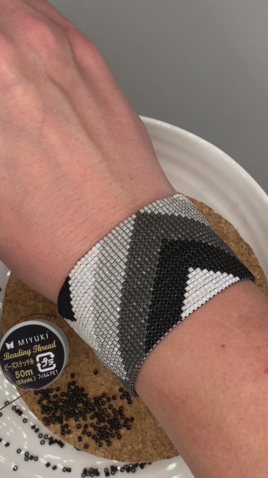 Video of a black, grey, and white beaded bracelet with chevron pattern on a cork and white plate.