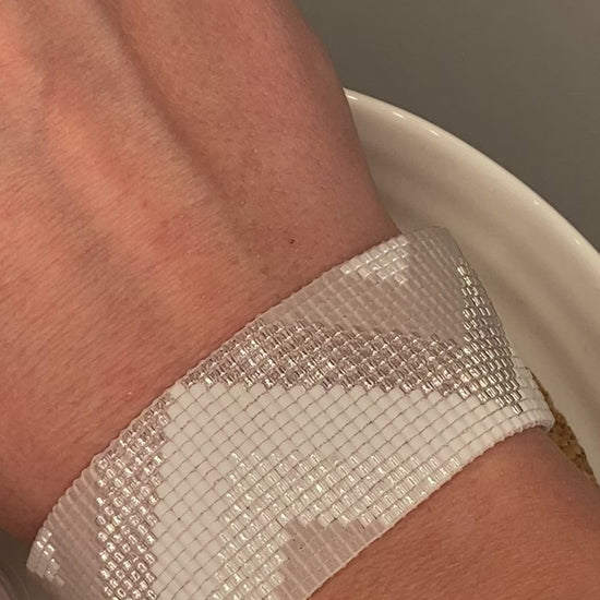 Video of a white, pearl, and crystal beaded bracelet with chevron pattern on a cork and white plate.