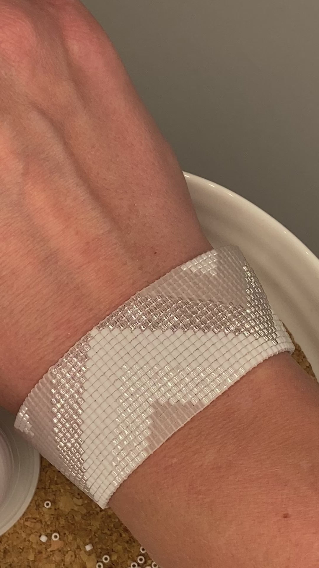 Video of a white, pearl, and crystal beaded bracelet with chevron pattern on a cork and white plate.