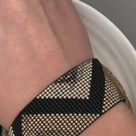 Video of a black and gold beaded bracelet with a chevron pattern on a white and cork plate.