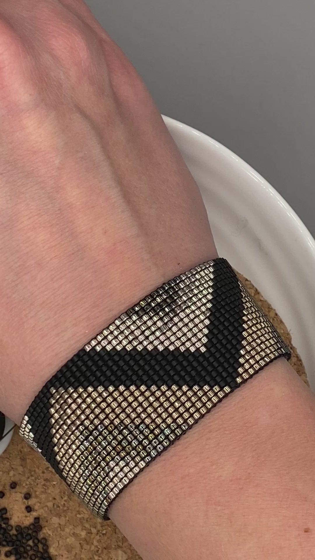 Video of a black and gold beaded bracelet with a chevron pattern on a white and cork plate.